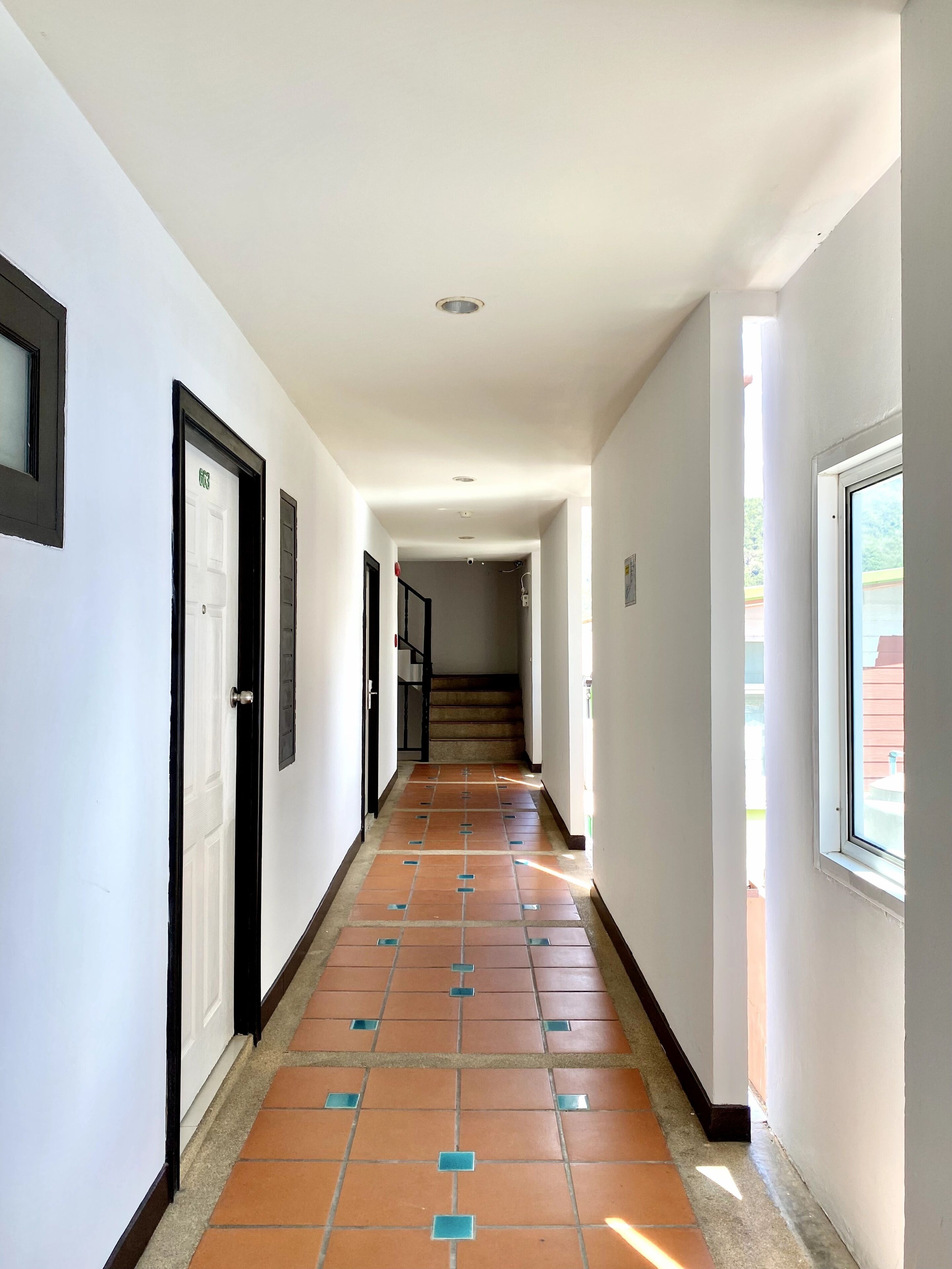 A hallway with white walls, a tiled floor, and a door marked with an exit sign.