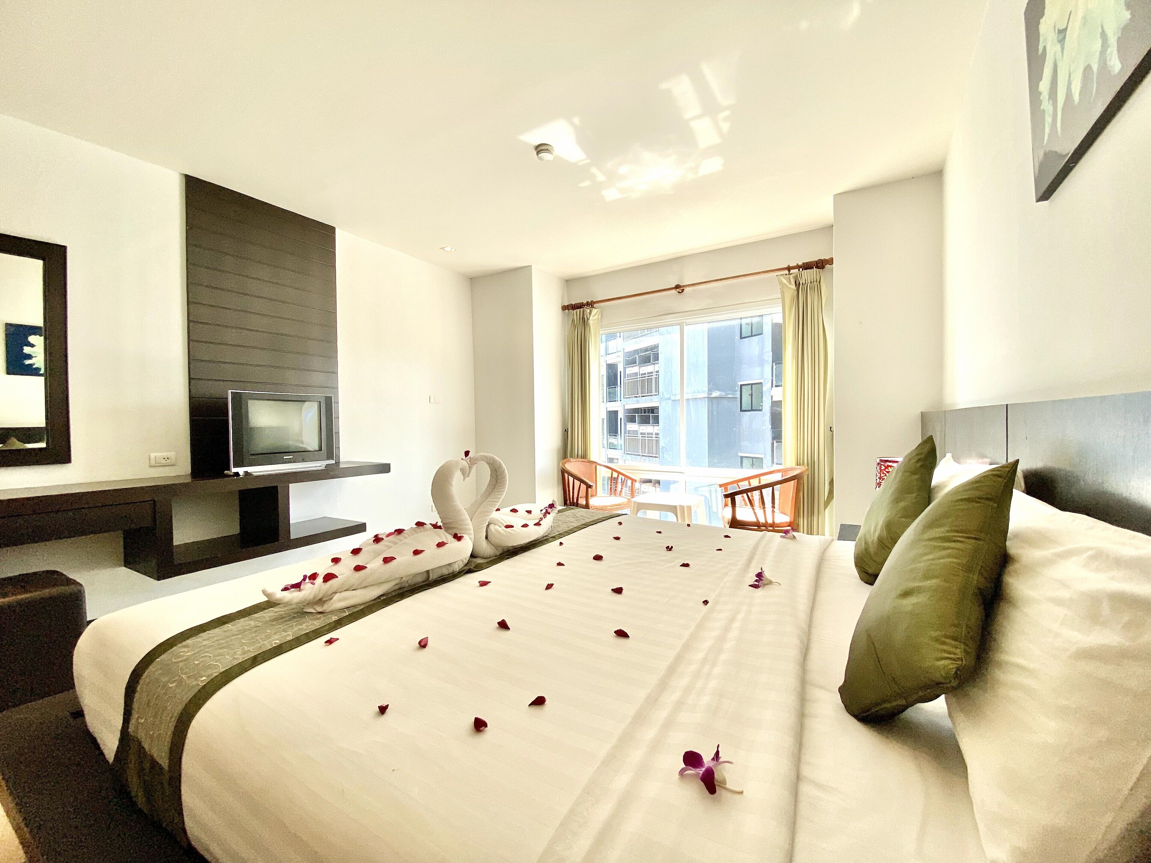 A hotel room with a bed, a TV, a balcony, and a view of the city.