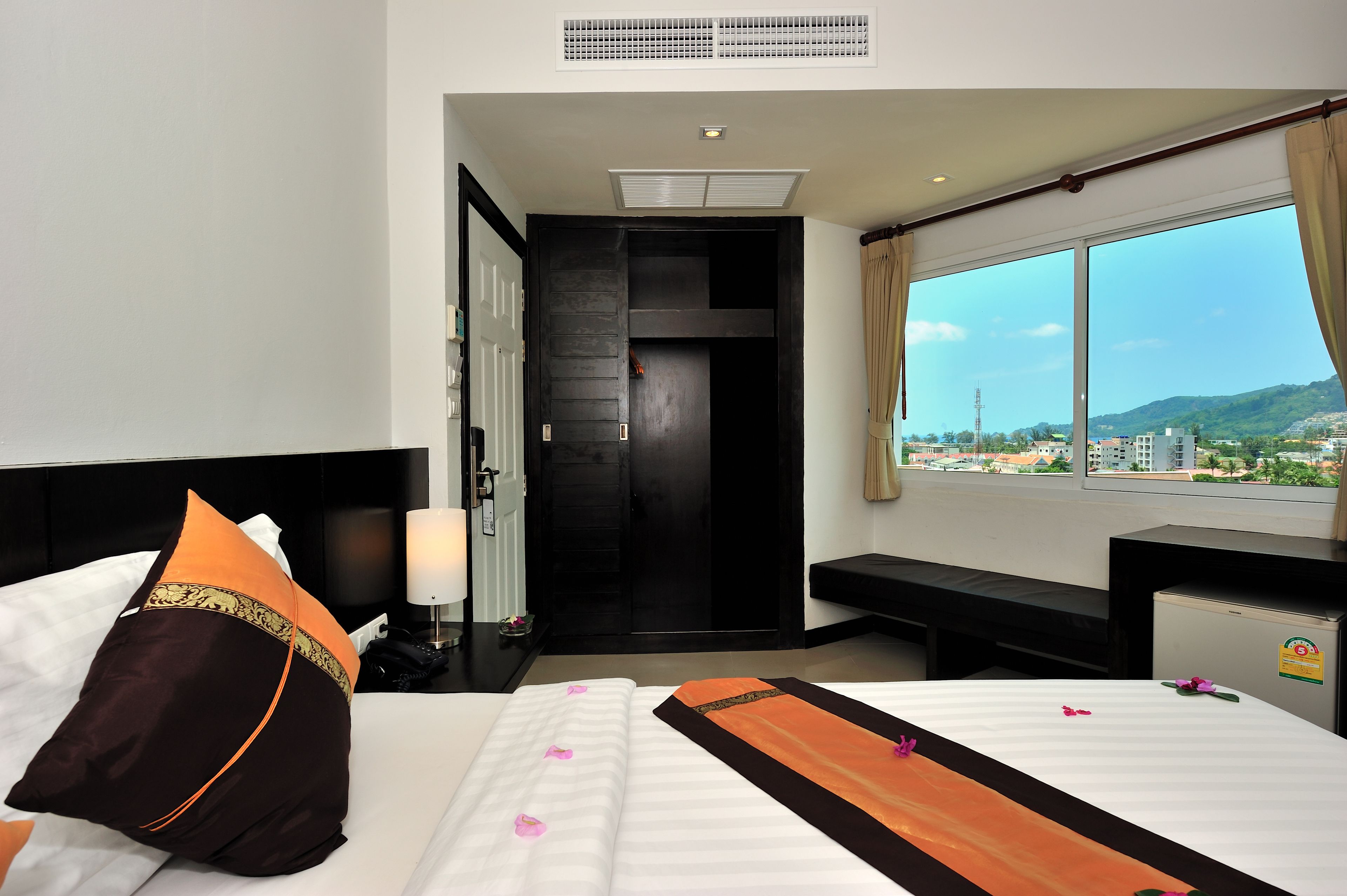 Una habitación de hotel con cama, escritorio, banco y un amplio ventanal con vistas a la ciudad.