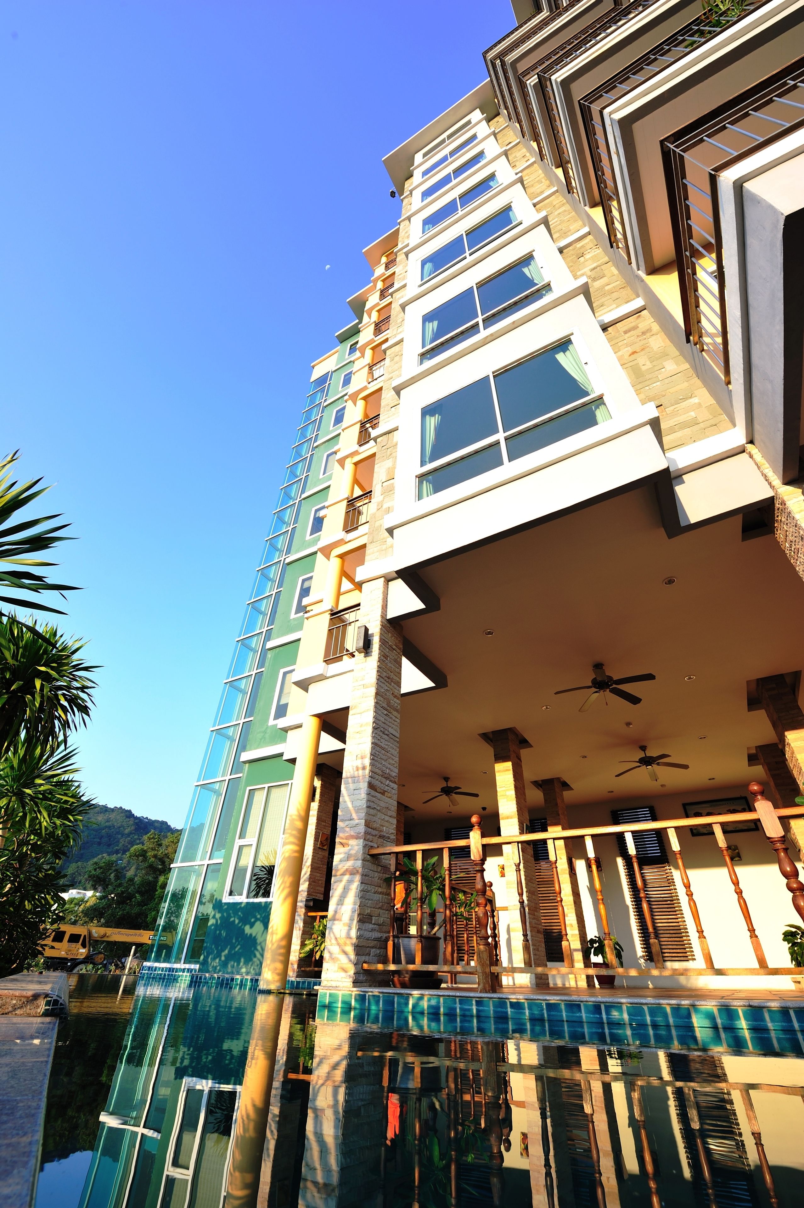 A multi-story hotel with balconies, a swimming pool, and a clear blue sky.