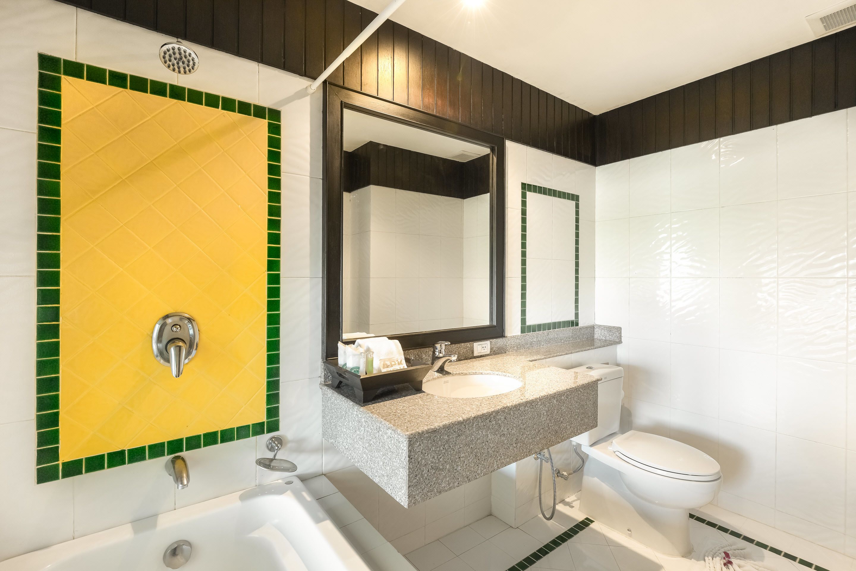 A bathroom with a yellow and green tiled wall, a sink, a toilet, and a bathtub.