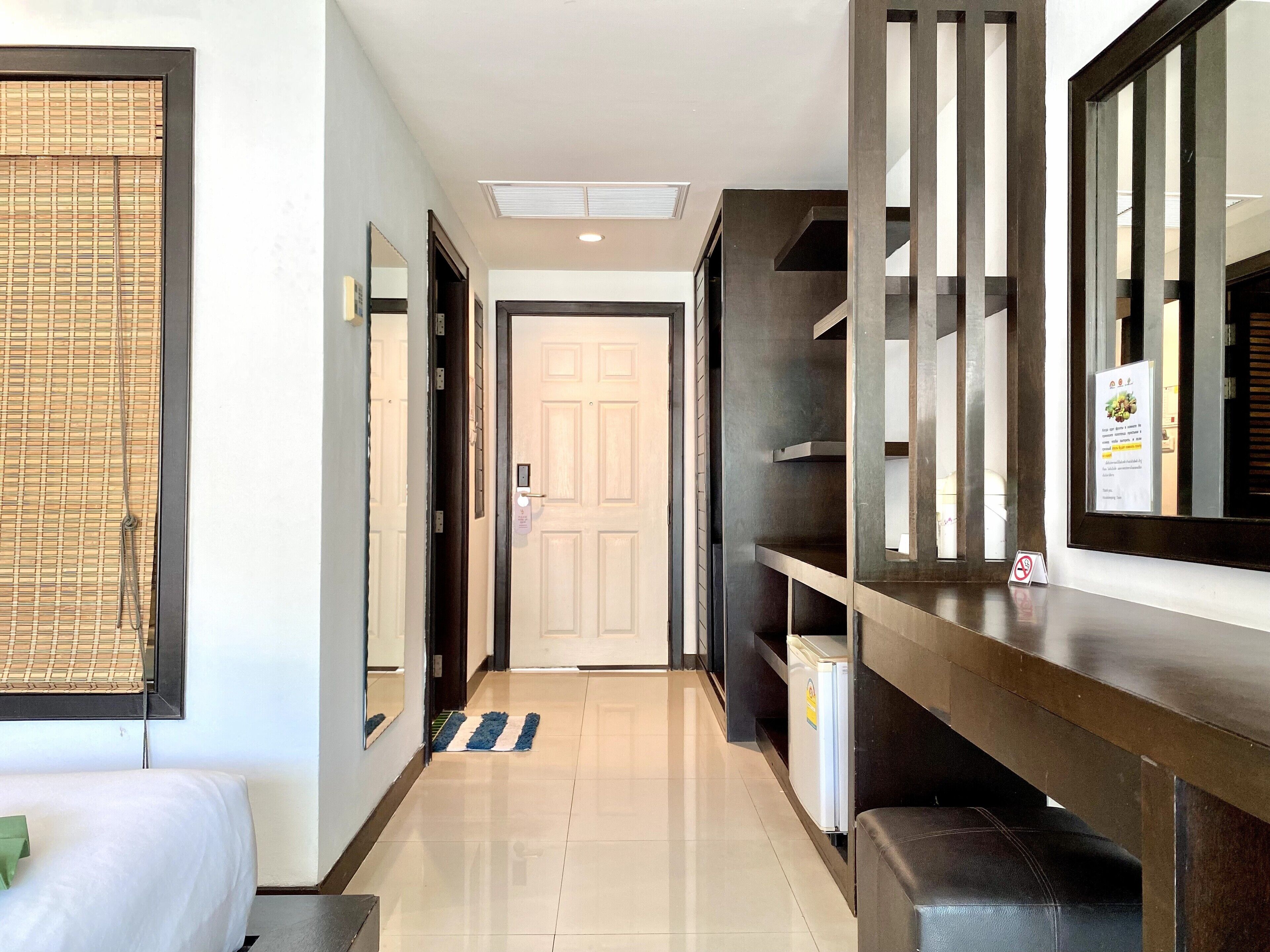 A hotel hallway with a bed, a mirror, a door, and a refrigerator.