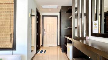 A hotel hallway with a bed, a mirror, a door, and a refrigerator.
