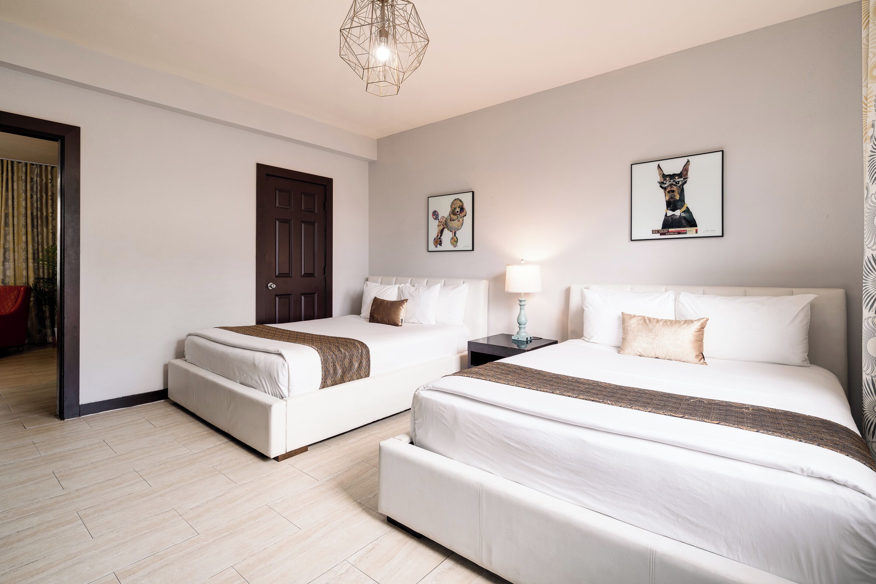 A hotel room with two beds, a wooden floor, a door, and a framed picture on the wall.