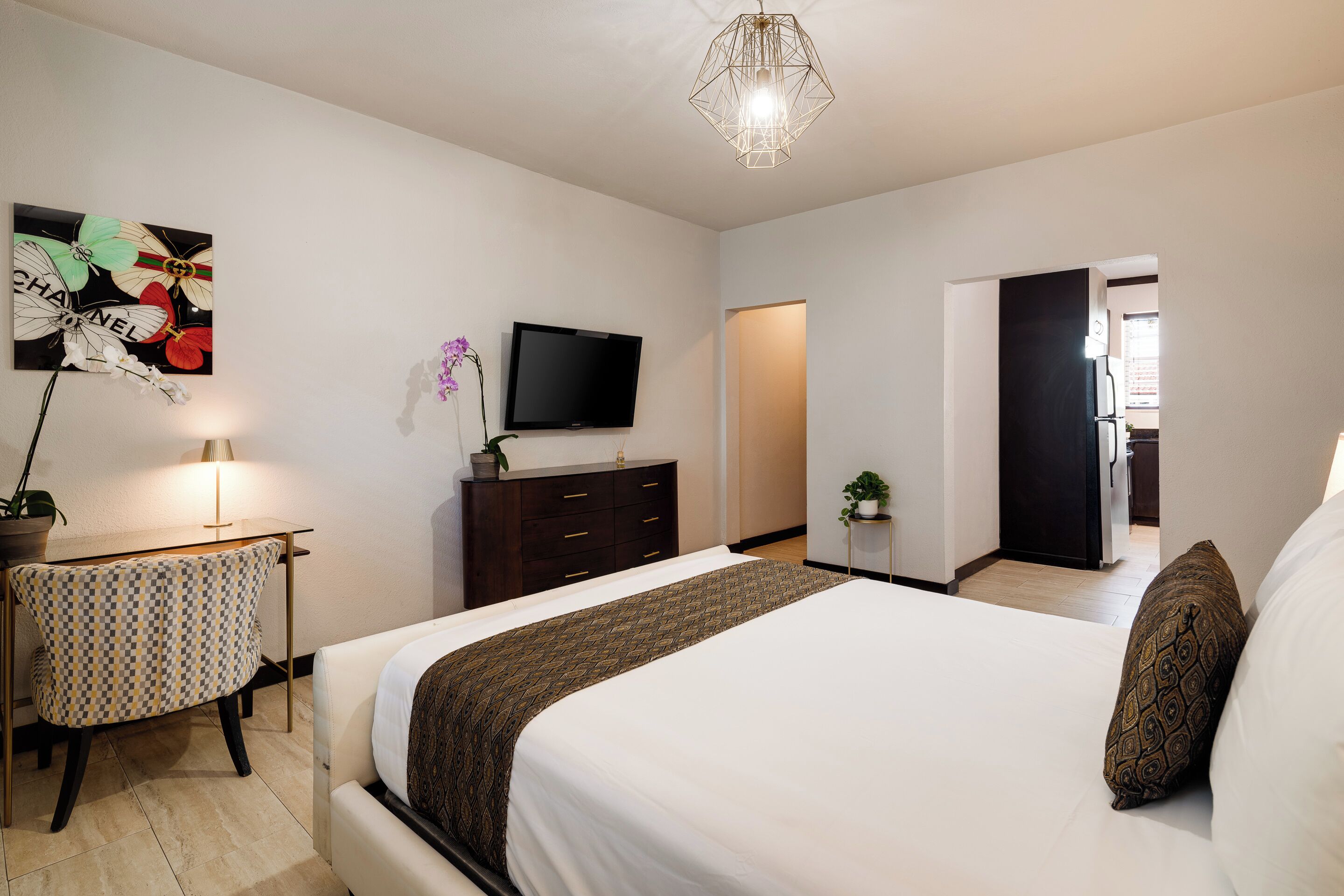 Ein modernes Schlafzimmer mit einem großen Bett, einem Flachbildfernseher, einem Schreibtisch mit Lampe und einem dekorativen Wandbild.