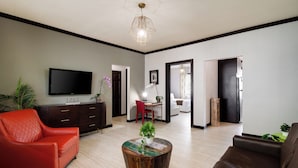 A modern living room with a flat-screen TV, a red leather sofa, a brown leather sofa, a wooden coffee table with a plant, and a dining area with a red chair. - Tradewinds Apartment Hotel (Miami Beach)