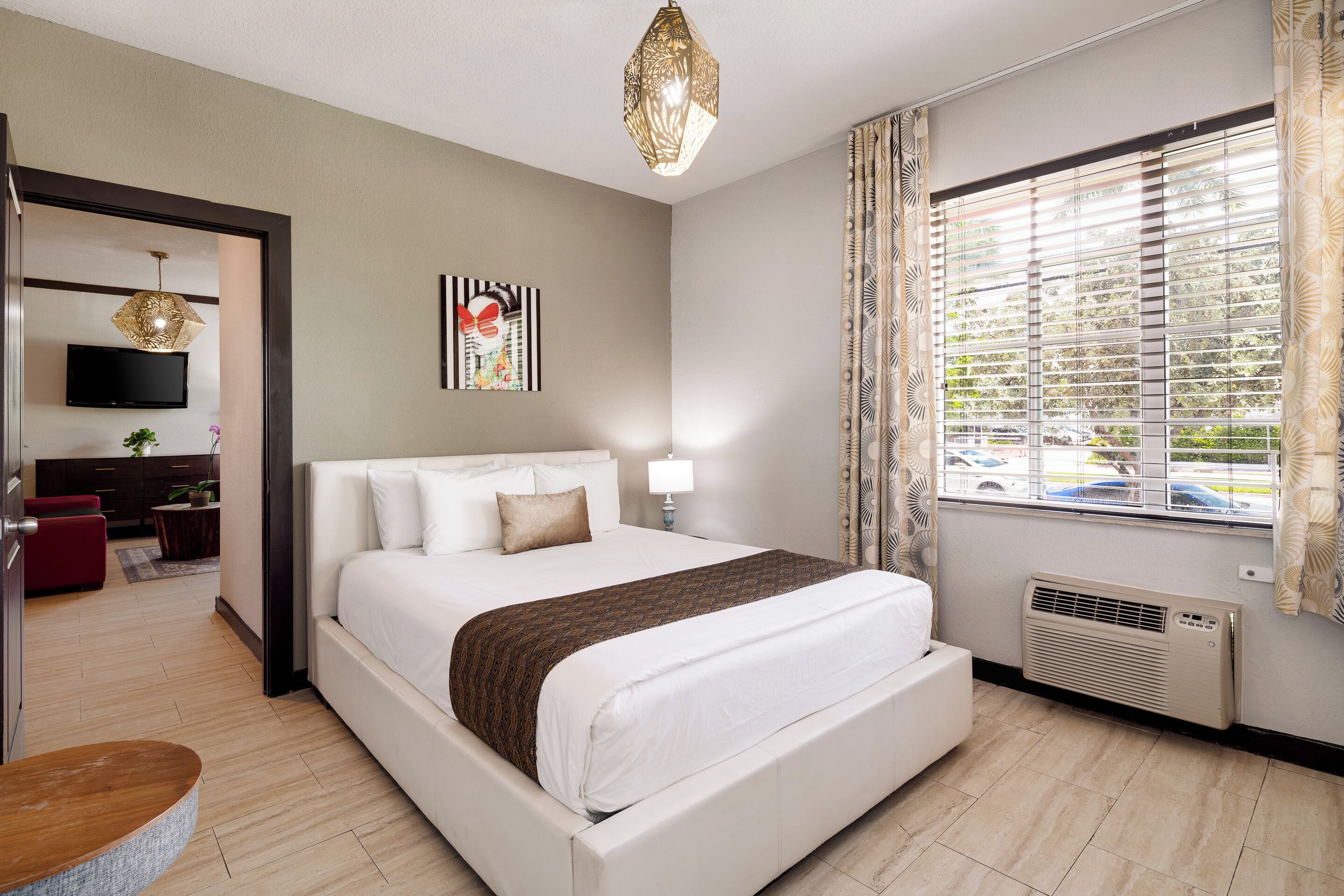 Une chambre d’hôtel moderne dotée d’un grand lit, d’un téléviseur à écran plat, d’un élément décoratif mural et d’une fenêtre avec des stores.