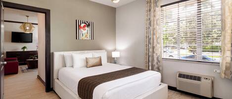 Une chambre d’hôtel moderne dotée d’un grand lit, d’un téléviseur à écran plat, d’un élément décoratif mural et d’une fenêtre avec des stores.