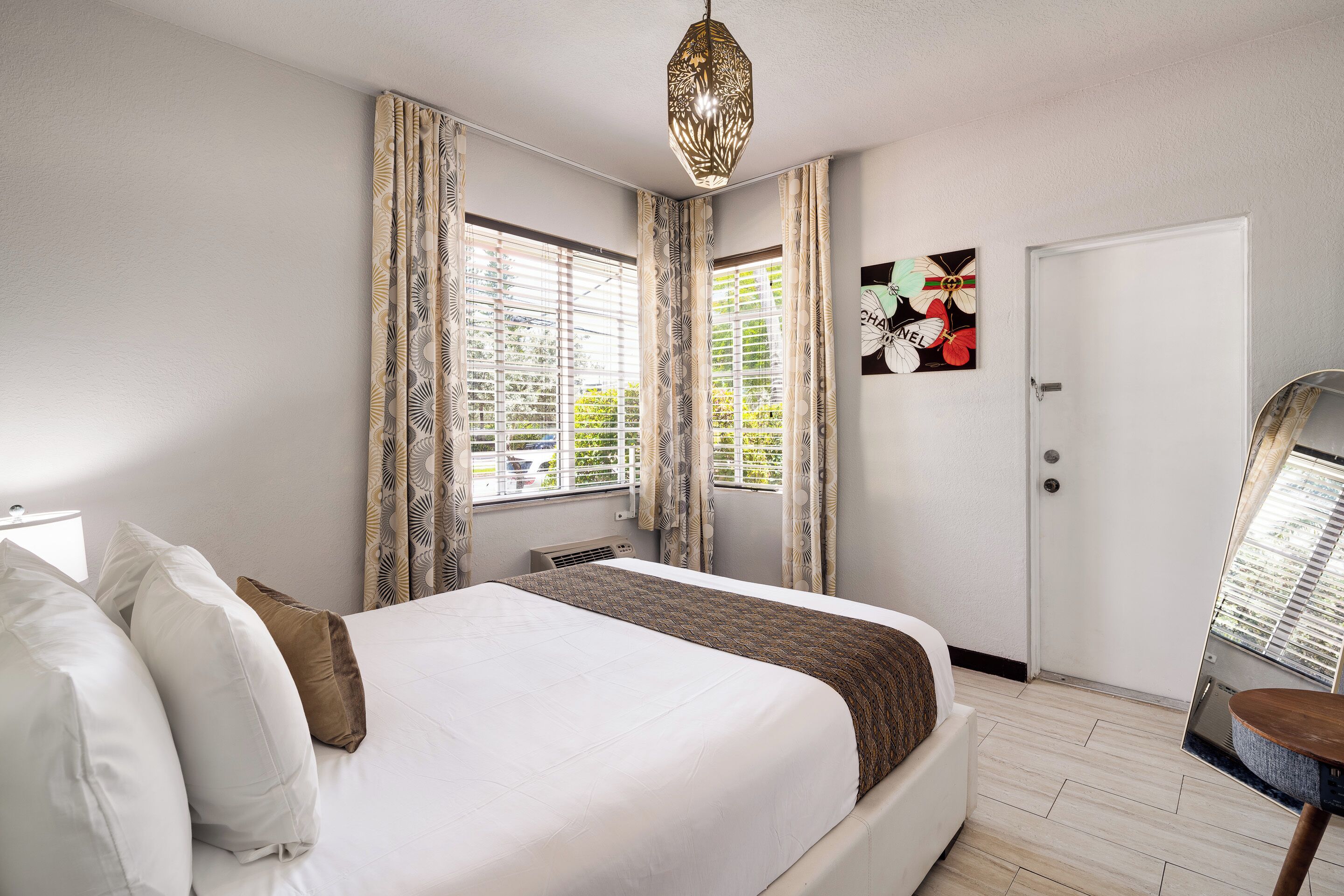 A hotel room with a large bed, a ceiling light, a door, and a window with curtains.