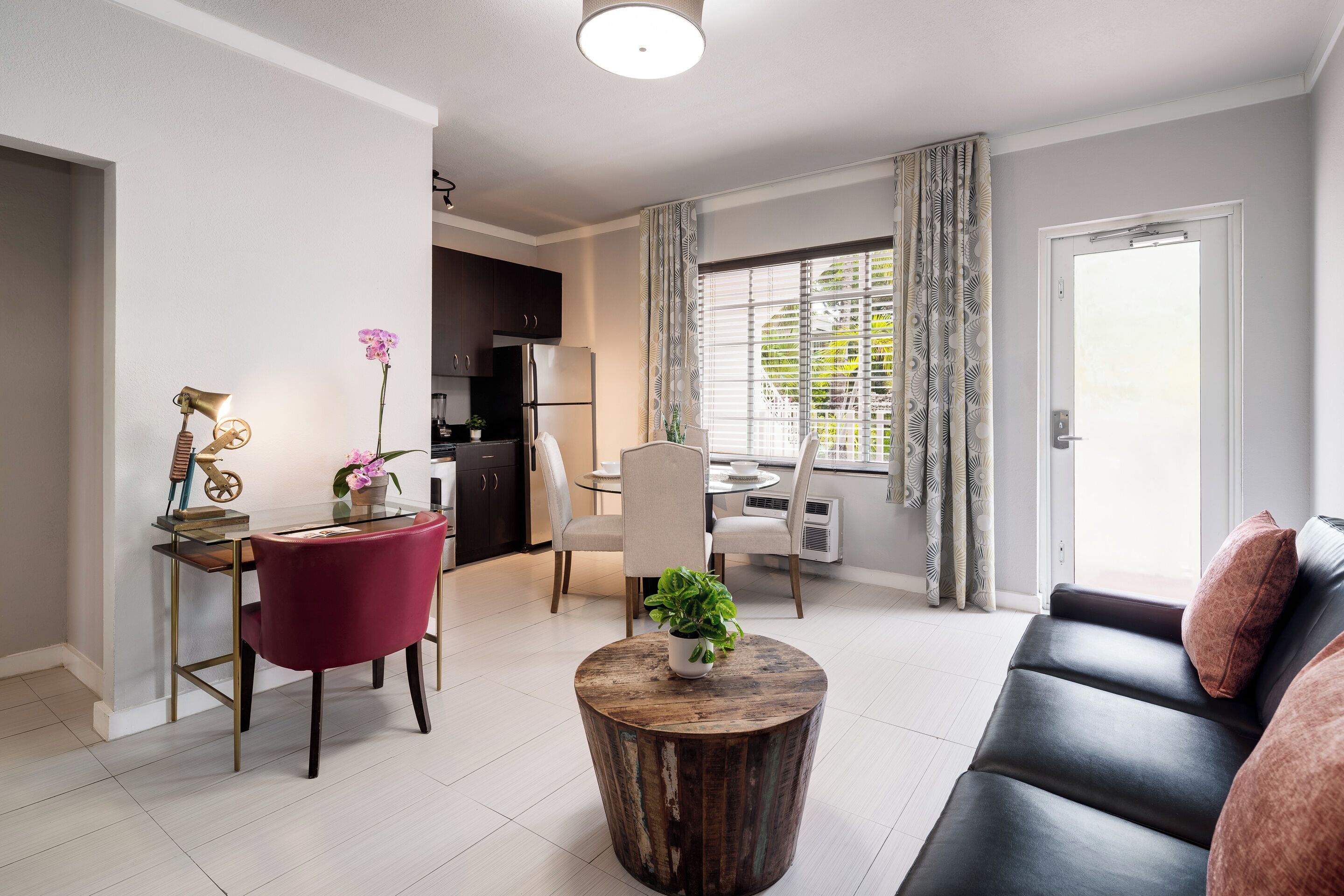 A modern living room with a sofa, a round coffee table, a red chair, and a dining area with a table and chairs.