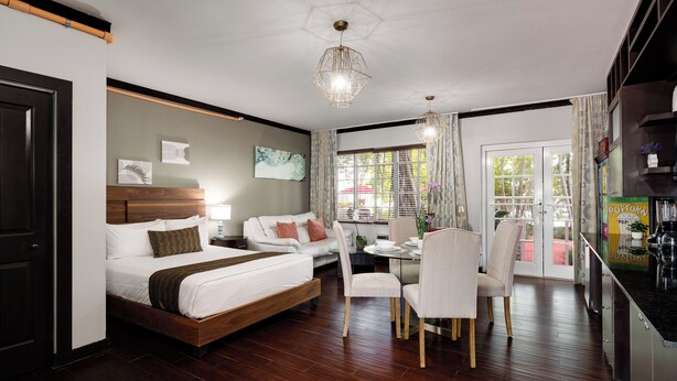 A modern hotel room with a wooden bed, a dining table with chairs, and a kitchen area. - Tradewinds Apartment Hotel (Miami Beach)
