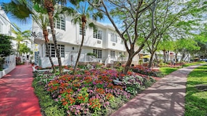 A white building with a red pathway and a flower garden in front. - Tradewinds Apartment Hotel (Miami Beach)