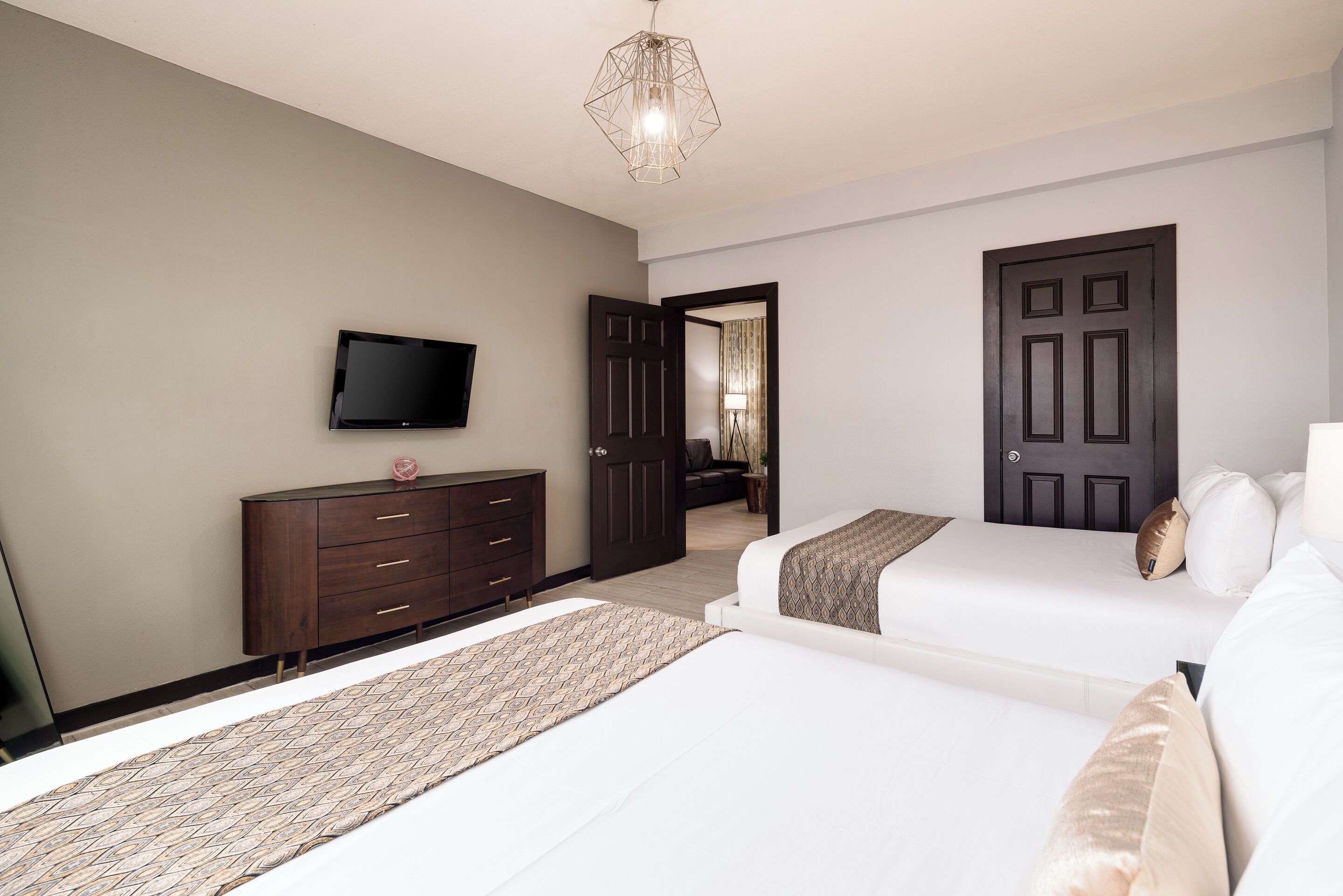 A hotel room with two beds, a TV, a dresser, and a door leading to another room.