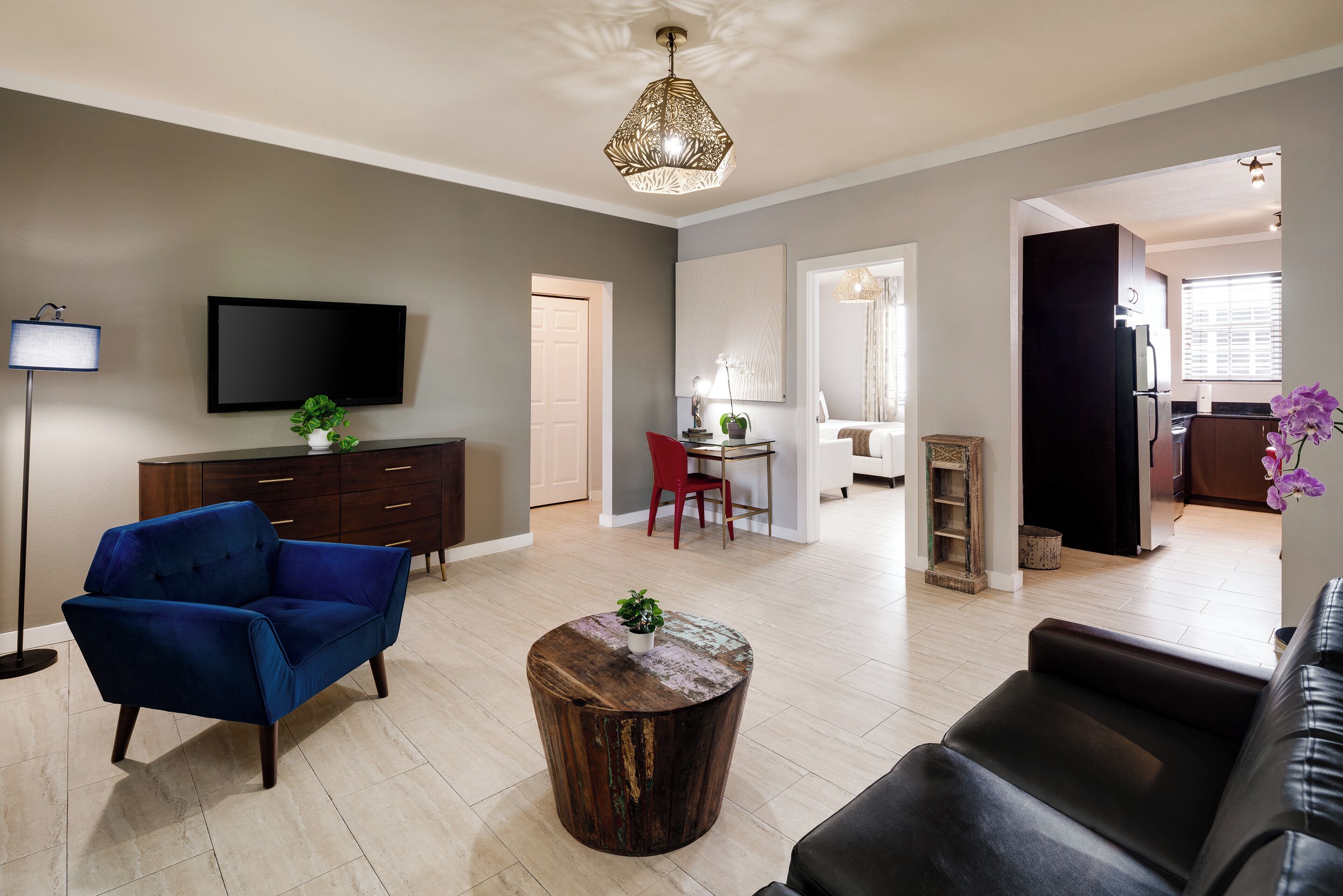 A modern living room with a blue sofa, a wooden coffee table, a flat-screen TV, and a dining area with a red chair.