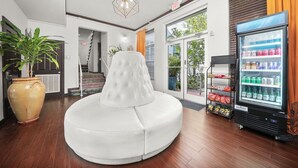 A modern interior with a white cushioned seating area, a vending machine, and a large potted plant. - Tradewinds Apartment Hotel (Miami Beach)