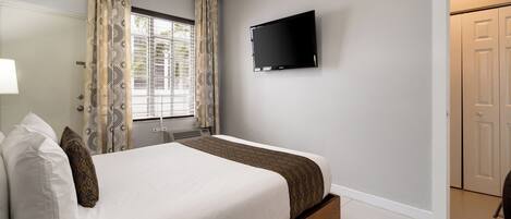 Un dormitorio con una cama, un televisor montado en la pared y una ventana con cortinas.