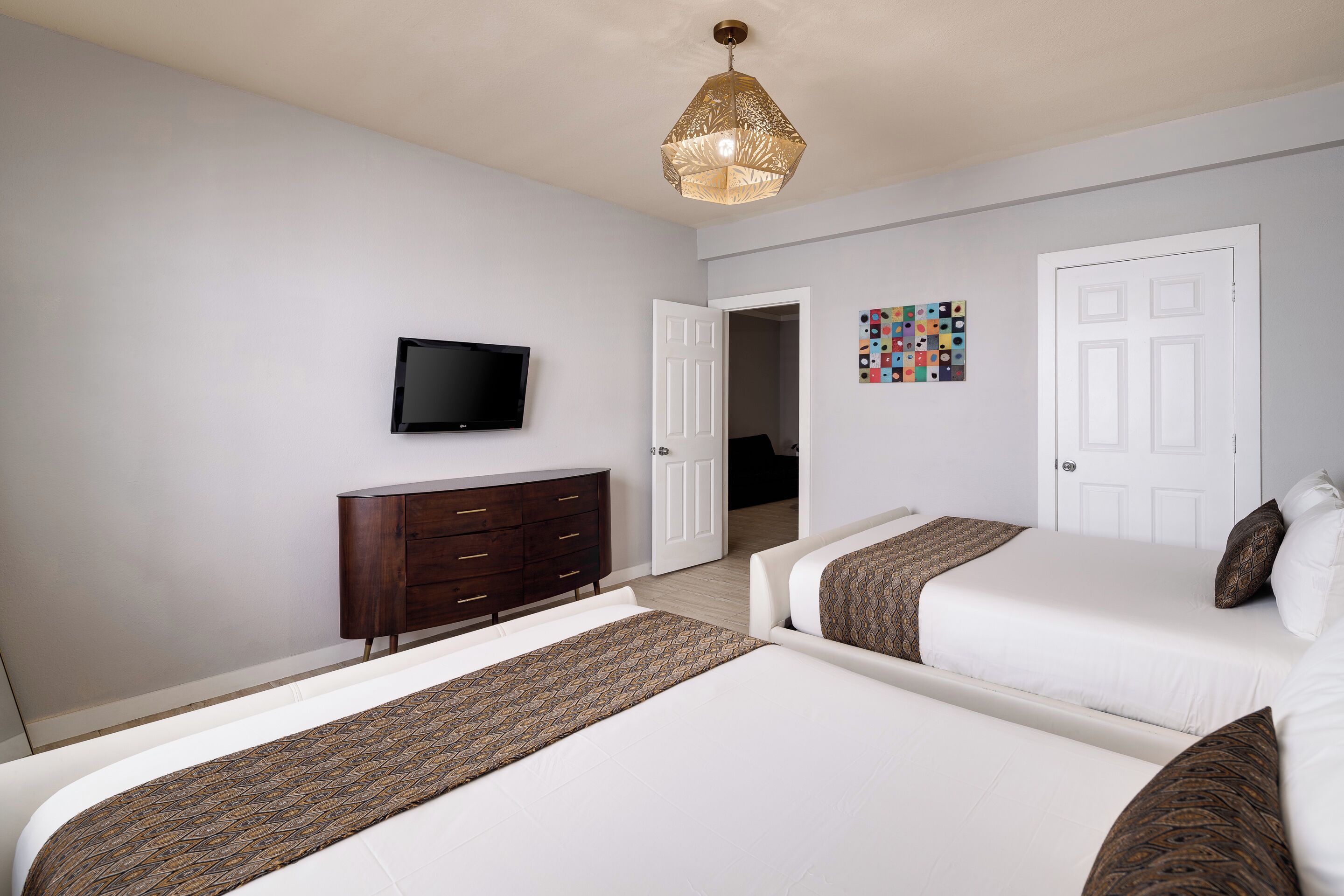 A hotel room with two beds, a TV, a dresser, and a door leading to another room.