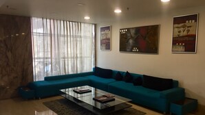 A modern living room with a teal sectional sofa, a glass coffee table, and artwork on the walls.