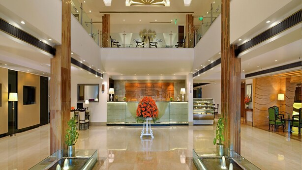 A spacious lobby with a central reception desk, a glass fountain, and a second-floor balcony with seating.