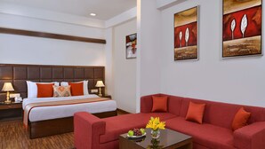 A hotel room with a large bed, a red sofa, a small table with flowers, and artwork on the walls.