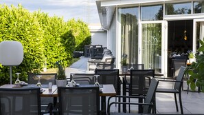 An outdoor patio area with tables and chairs, a large potted plant, and a view into the building.