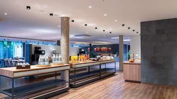A modern hotel lobby with a reception desk, seating area, and a buffet with various food and drink options.