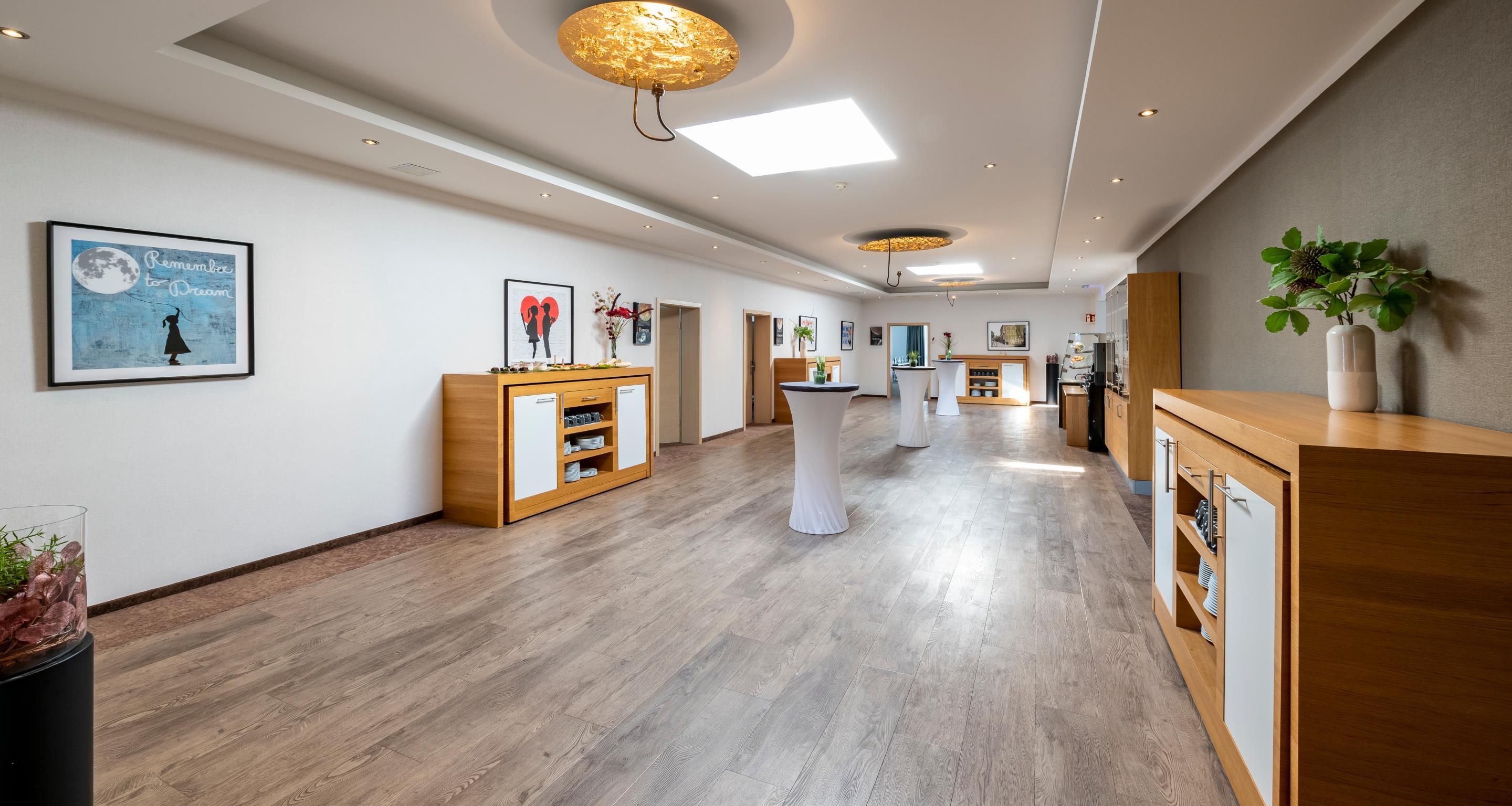 A hotel corridor with wooden flooring, white reception desks, and artwork on the walls.