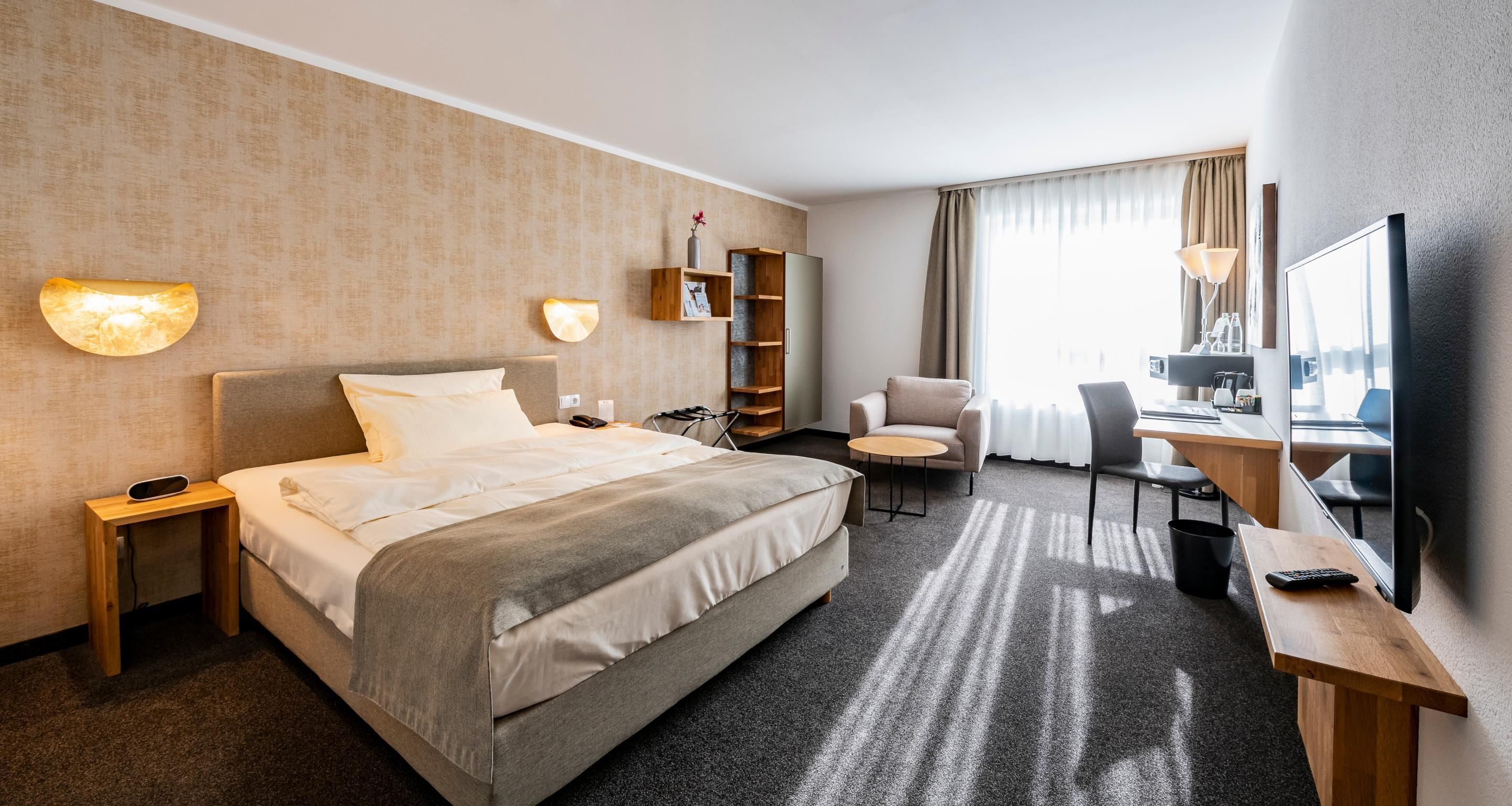 Una habitación de hotel con cama, mesita de noche, lámpara, silla, escritorio y un espejo grande.