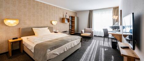 Una habitación de hotel con cama, mesita de noche, lámpara, silla, escritorio y un espejo grande.