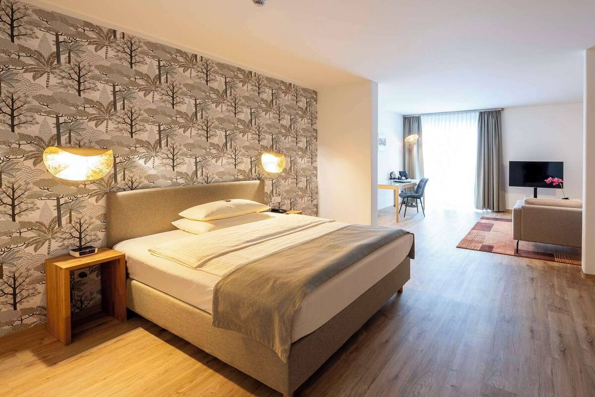 Ein Hotelzimmer mit Bett, Nachttischlampen, einem Schreibtisch mit Stuhl, einem Fernseher und einem Kleiderschrank.