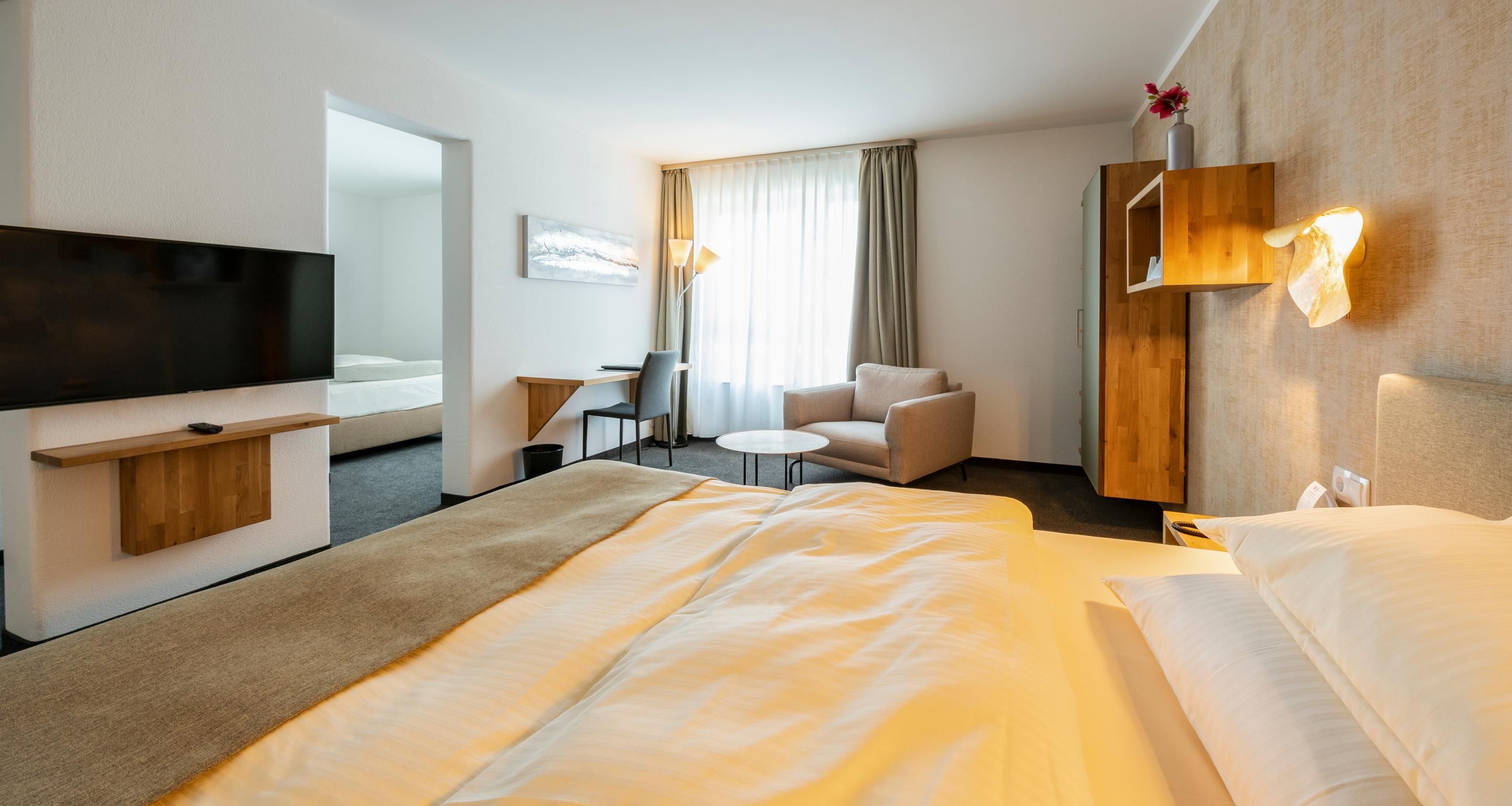 Una habitación de hotel con cama, escritorio, silla, televisor y ventana con cortinas.