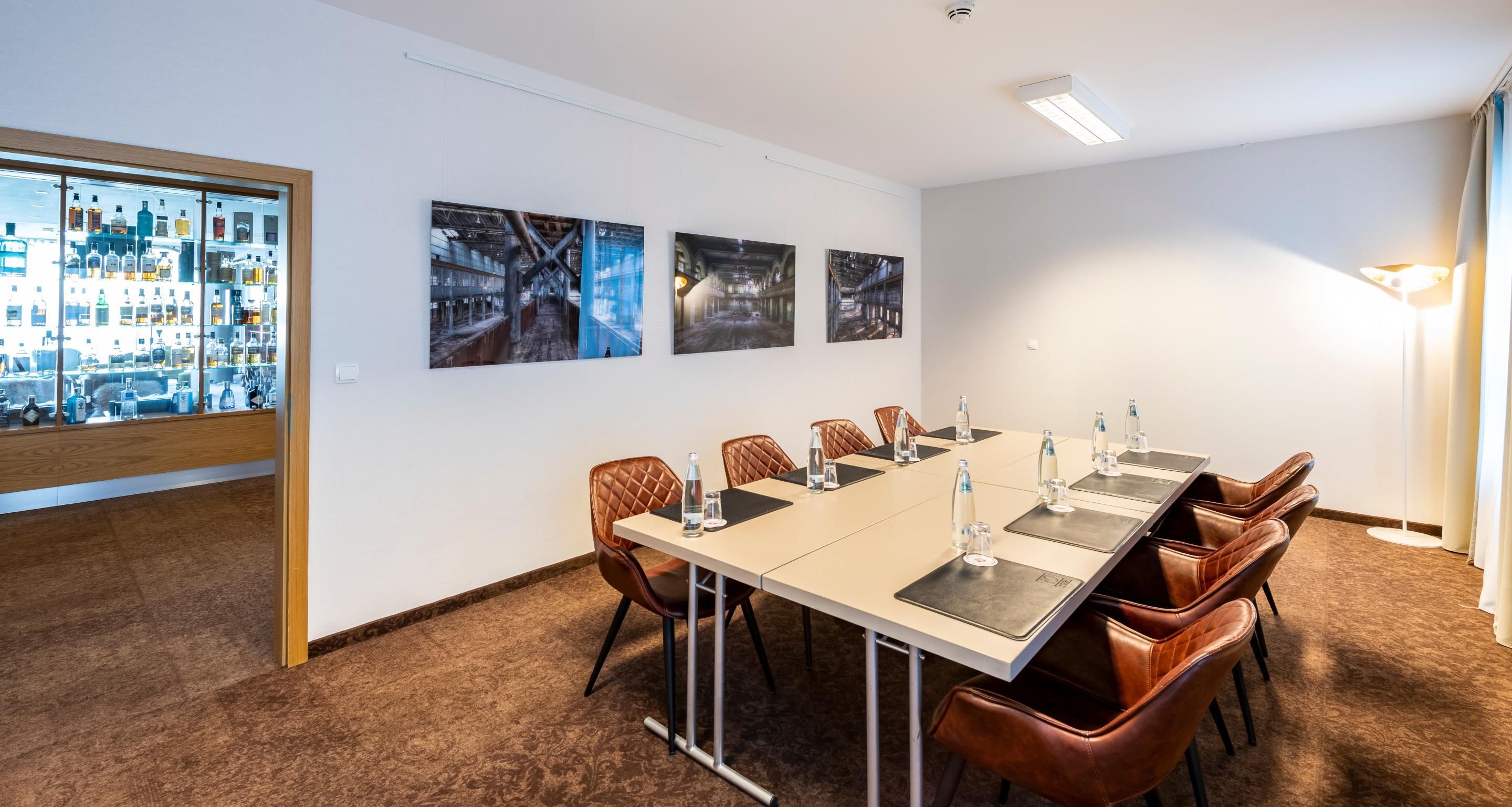 Un salón de conferencias con una larga mesa, sillas de cuero y vistas a un paisaje urbano a través de un muro de cristal.
