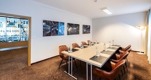 Un salón de conferencias con una larga mesa, sillas de cuero y vistas a un paisaje urbano a través de un muro de cristal.