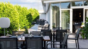 An outdoor patio with tables and chairs, a potted plant, and a glass door leading to an interior space. - Best Western Plus iO Hotel (Schwalbach am Taunus)