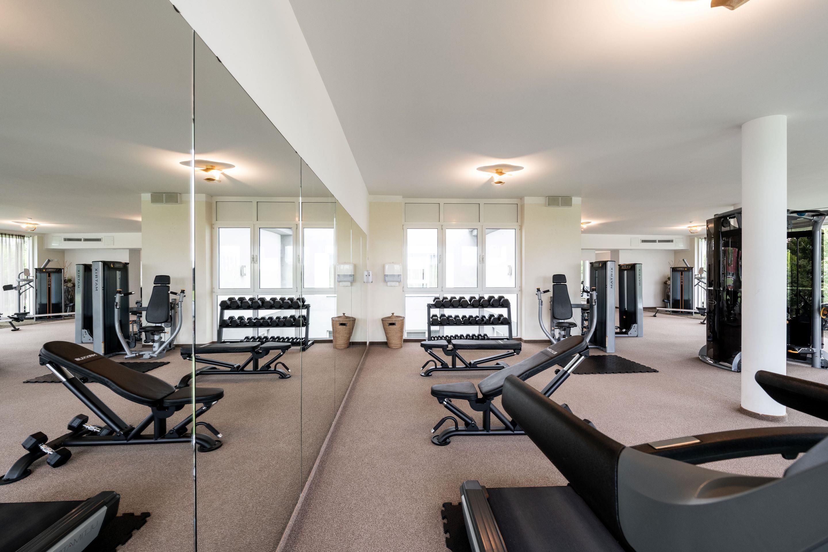 A gym with exercise equipment, mirrors, and windows.