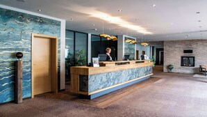 A reception area with a wooden counter, glass doors, and a modern chandelier. - Best Western Plus iO Hotel (Schwalbach am Taunus)
