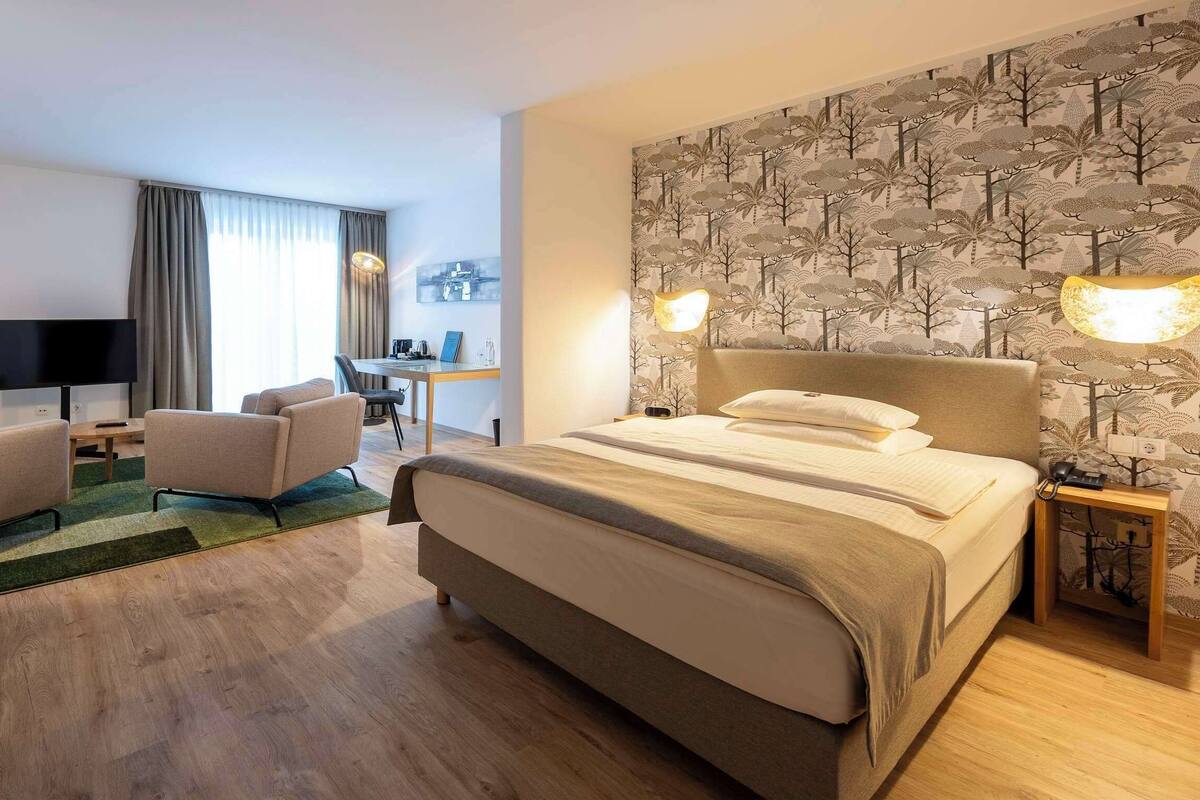 Ein Hotelzimmer mit einem großen Bett, einem Schreibtisch, einem Sessel und einem Fernseher.