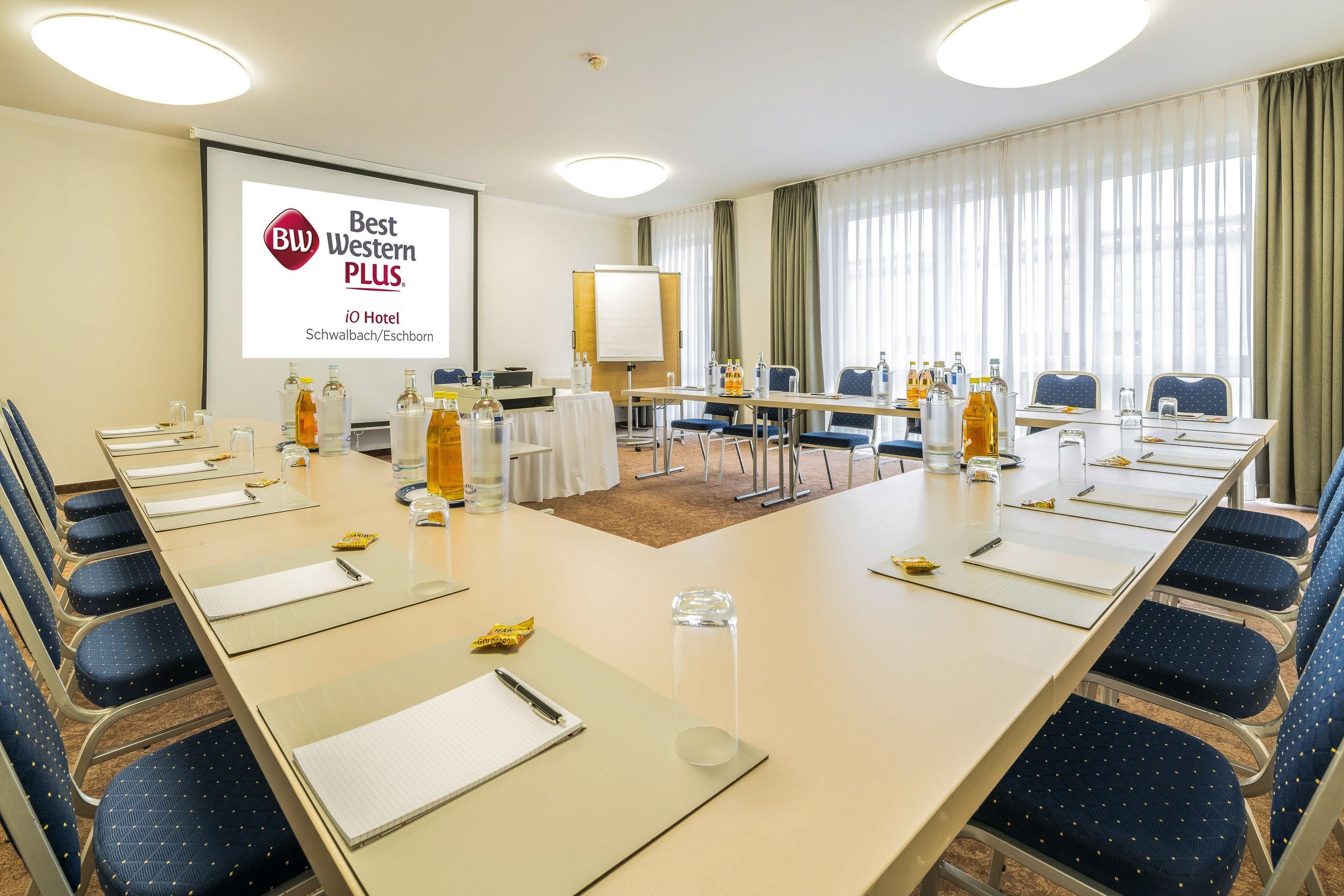 Une salle de conférence équipée d’une longue table, de chaises et d’un écran de projection affichant un logo.