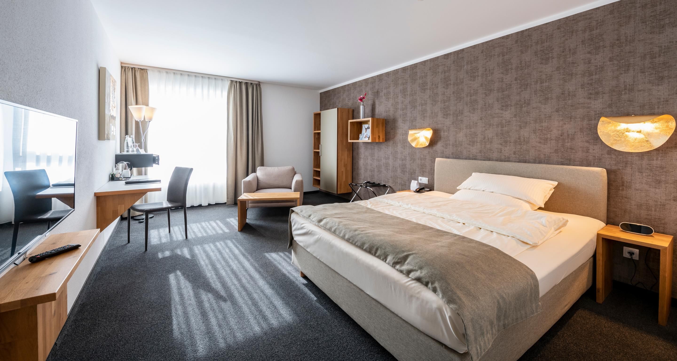 A hotel room with a bed, desk, chair, and a TV.