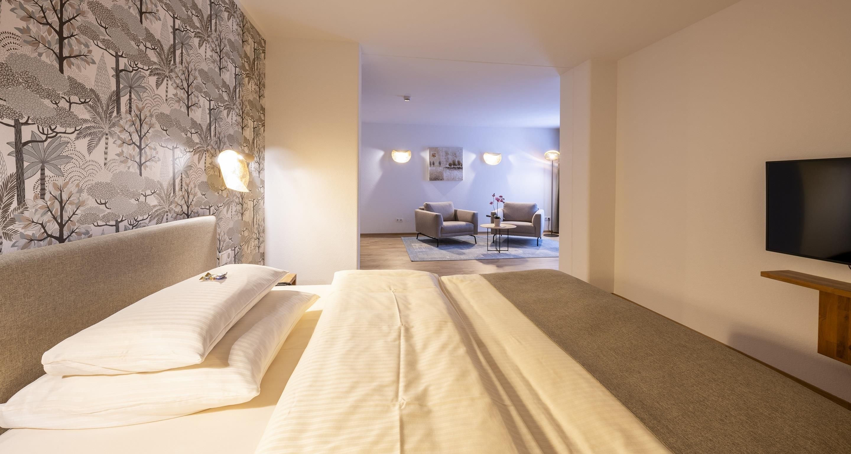 A hotel room with a bed, a TV, and a seating area with a table and chairs.