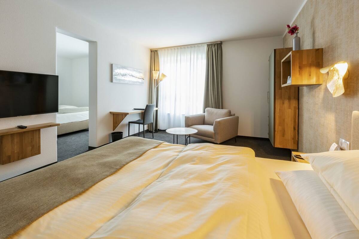 Ein Hotelzimmer mit Bett, Schreibtisch, Stuhl, Fernseher und einem Fenster mit Vorhängen.