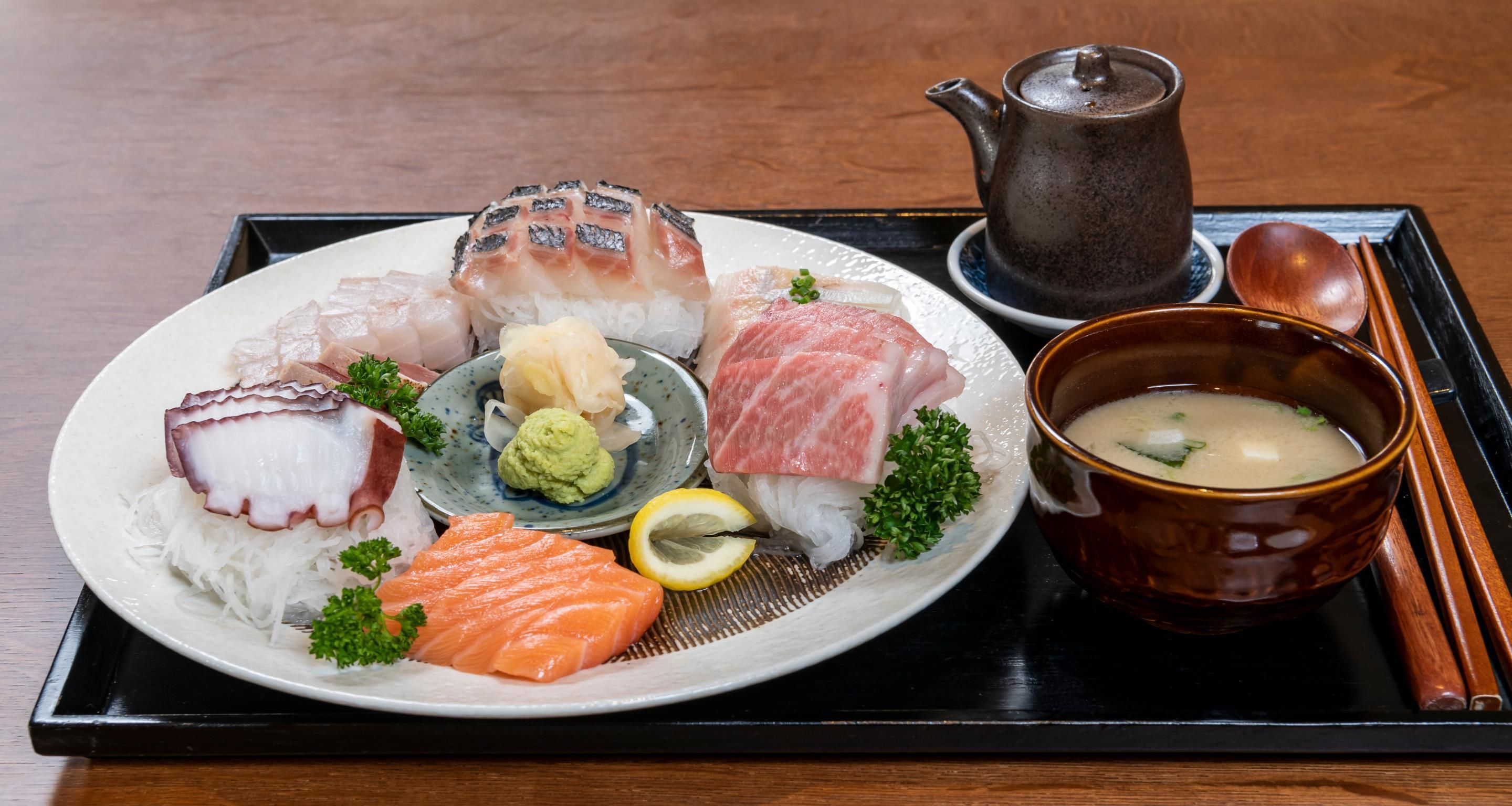 A traditional Japanese meal with sashimi, a bowl of soup, and a teapot on a tray.