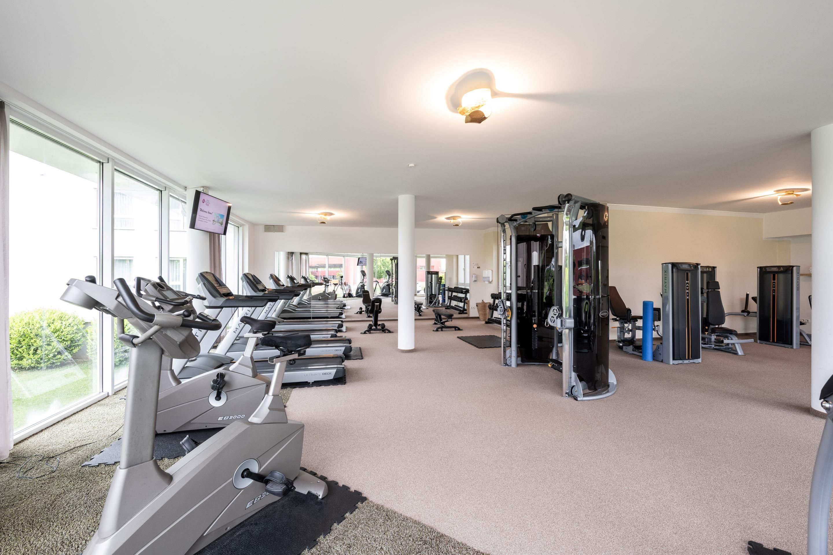 Ein Fitnessstudio mit Laufbändern, Kraftgeräten und einem Fernsehbildschirm.