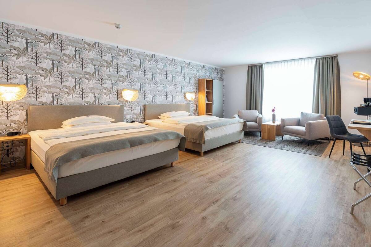 Ein Hotelzimmer mit zwei Betten, einem Schreibtisch, einem Stuhl, einem Fernseher und einem Fenster mit Vorhängen.