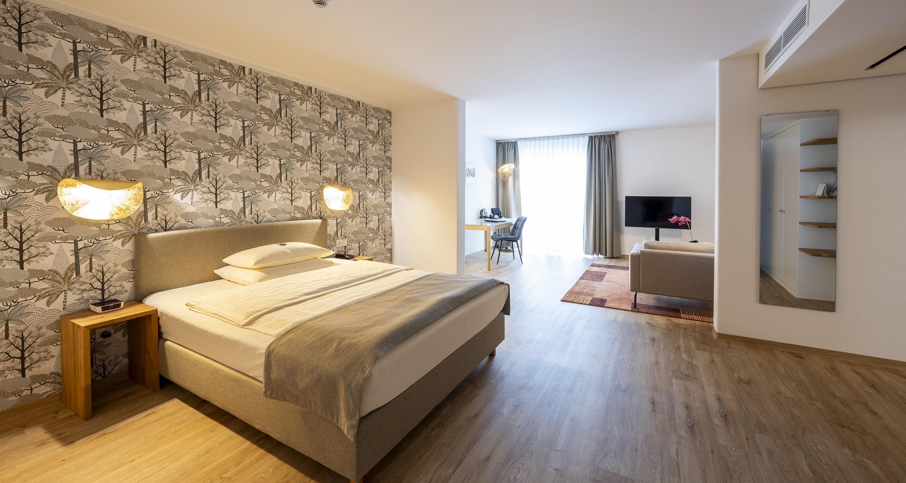 A hotel room with a bed, bedside lamps, a desk, a chair, a TV, and a wardrobe.