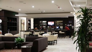 Eine Hotelhalle mit Barbereich, Sitzgelegenheiten und einer großen Topfpflanze.