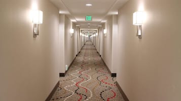 Un pasillo de hotel con alfombra estampada, apliques de pared y un letrero de salida.
