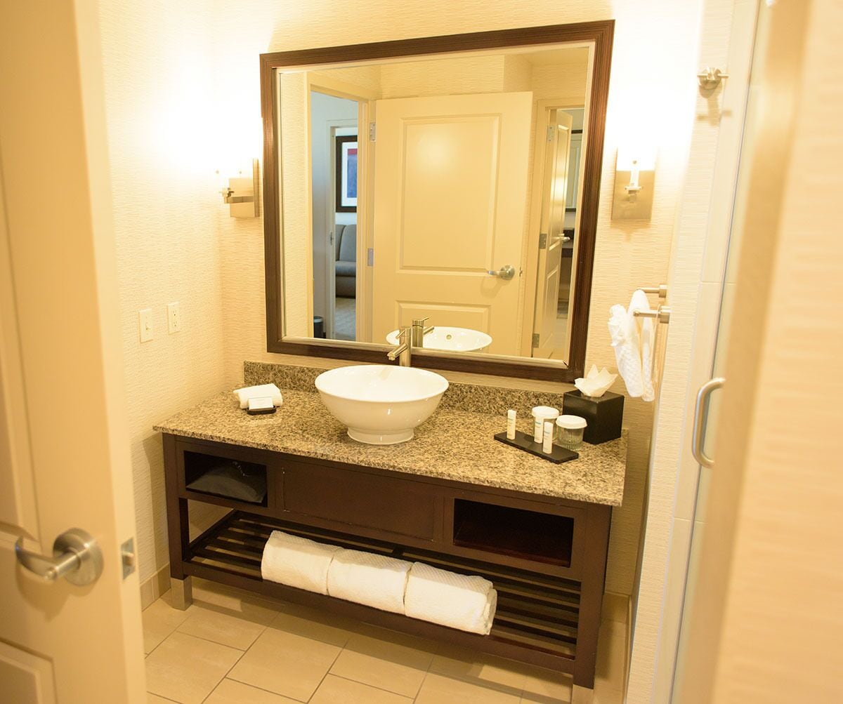 A hotel bathroom with a white sink, dark wooden vanity, and a large mirror.