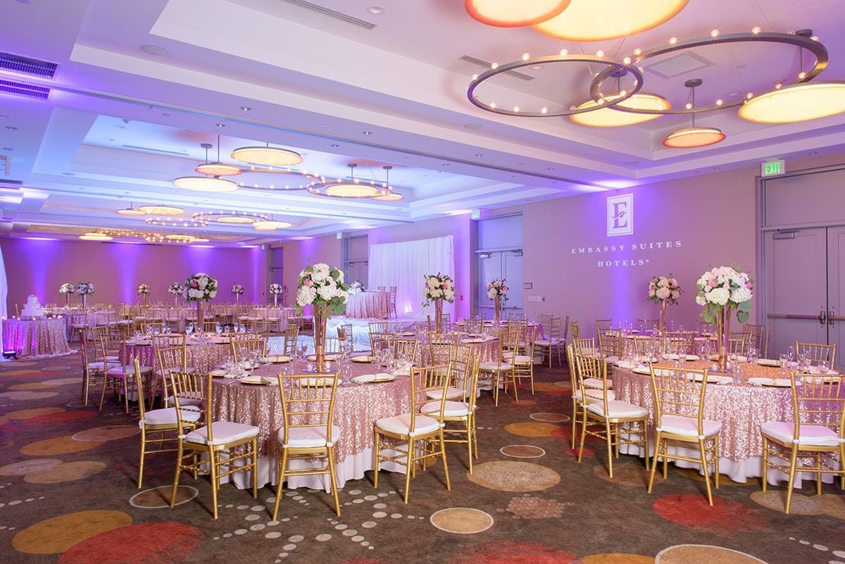 A banquet hall with round tables, gold chairs, and purple ambient lighting.