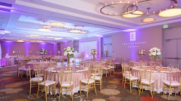 A banquet hall with round tables, gold chairs, and purple ambient lighting.